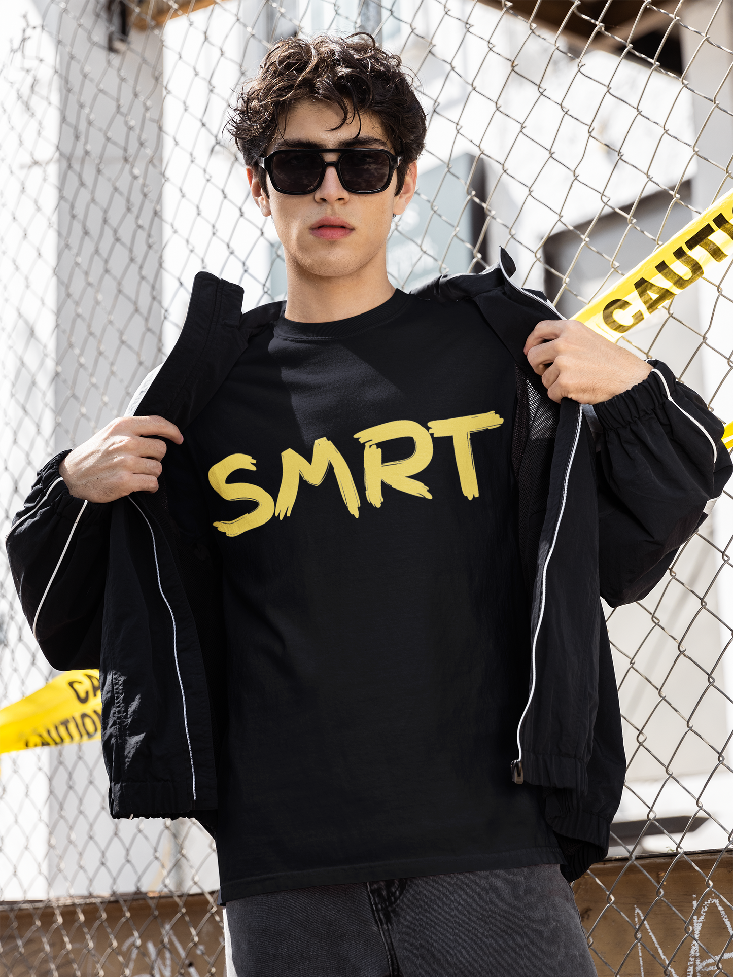 Man showing off black SMRT T-Shirt with yellow SMRT lettering, posing confidently near caution tape