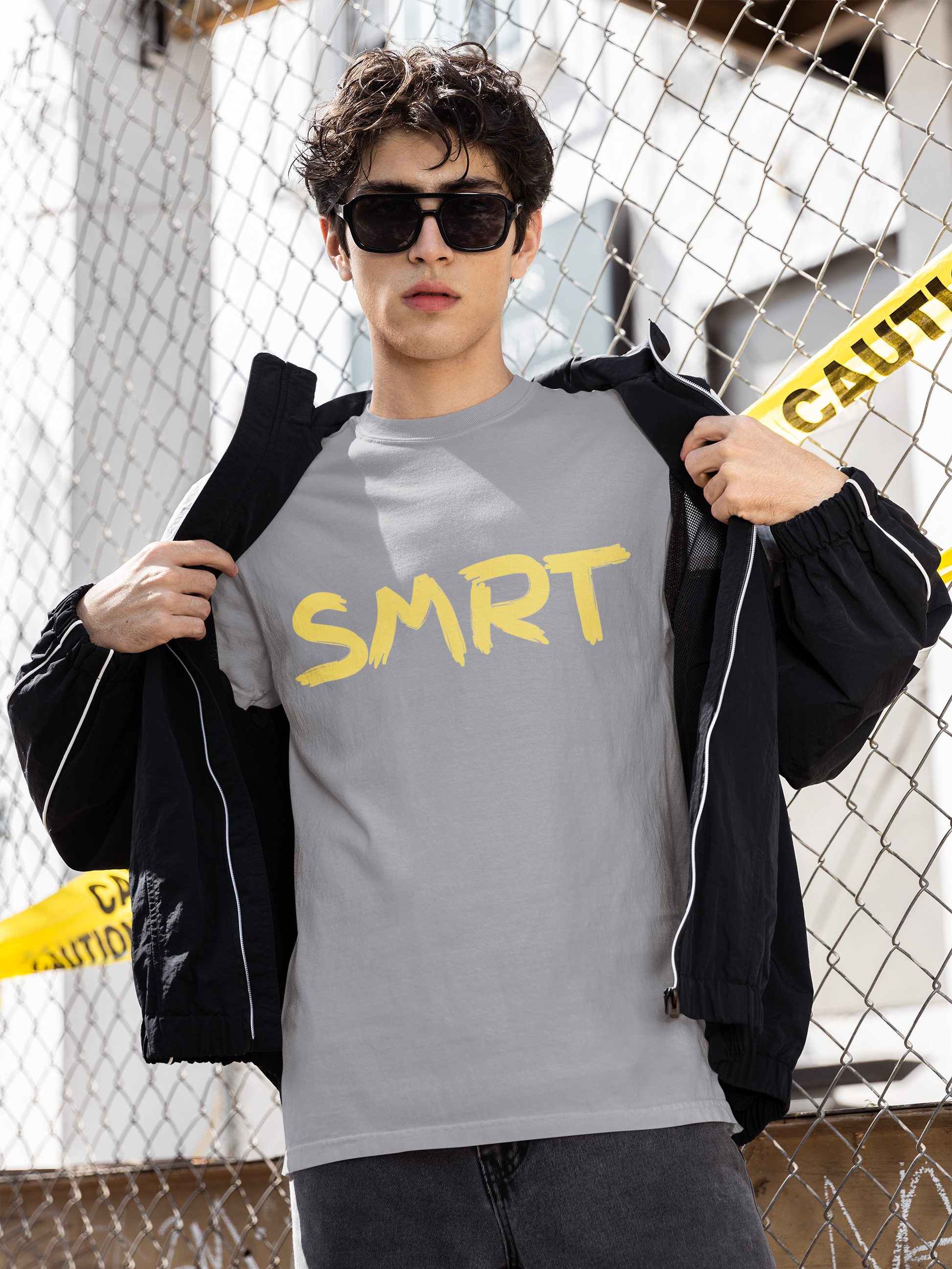 Man revealing grey SMRT T-Shirt with bold yellow SMRT text while standing in front of caution-taped fence