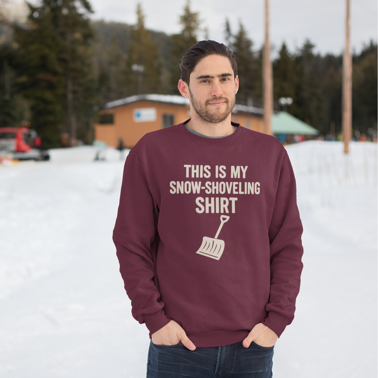 This Is My Snow-Shoveling Shirt – Funny Winter Chore Sweatshirt modeled outdoors in a snowstorm setting with winter cabins behind, highlighting cozy winter weather style