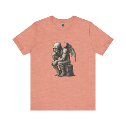 Peach-colored t-shirt with a black and white illustration of Cthulhu posed as Rodin's The Thinker.  The tee shirt is displayed on a hite background. 