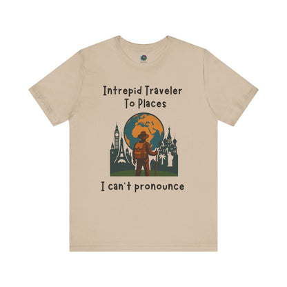 Beige t-shirt with travel-themed graphic and text "Intrepid Traveler to Places I Can't Pronounce" on a white background