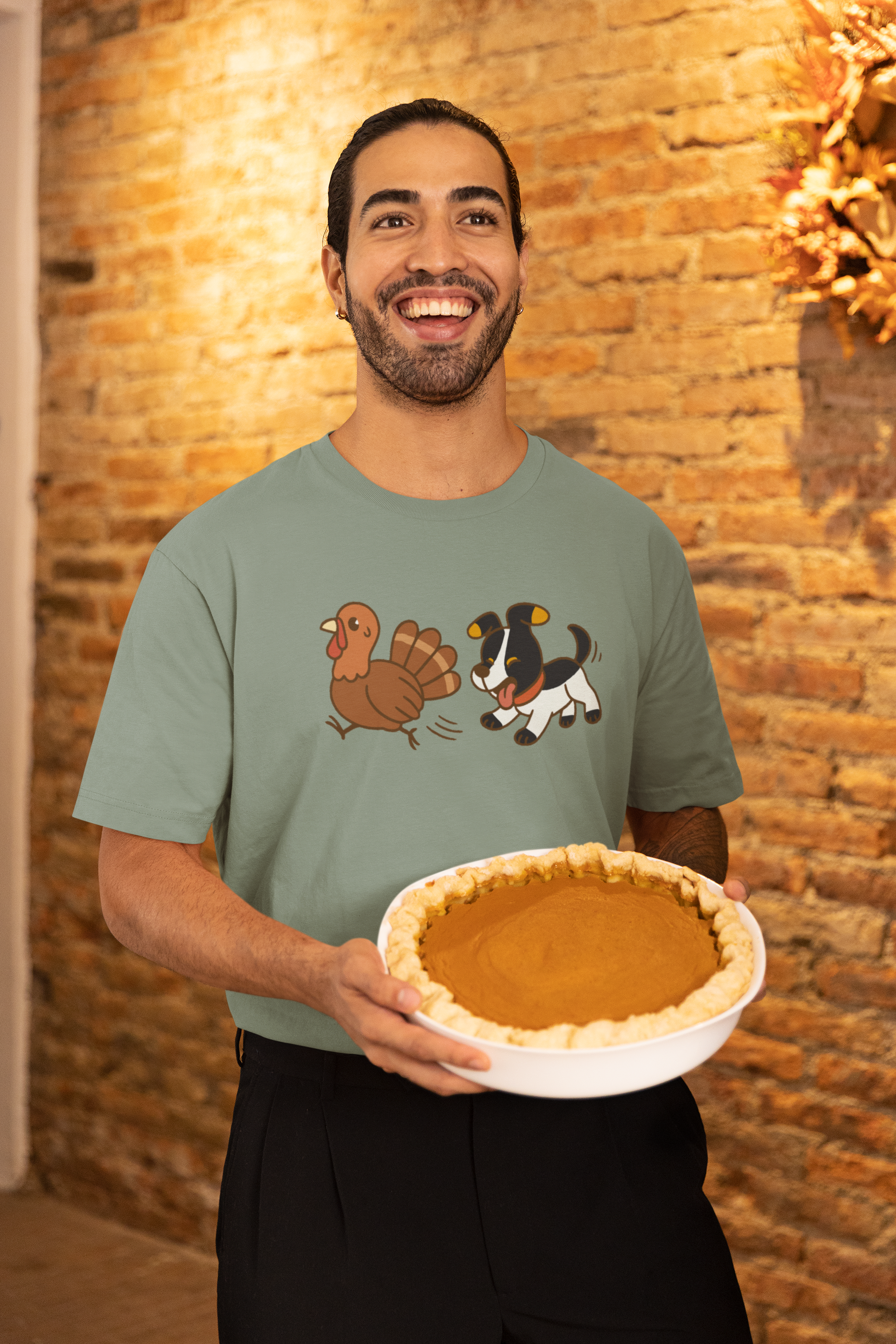 Dog Chasing Turkey T-Shirt – Funny Thanksgiving Dog Tee worn by man holding pumpkin pie in warm brick kitchen