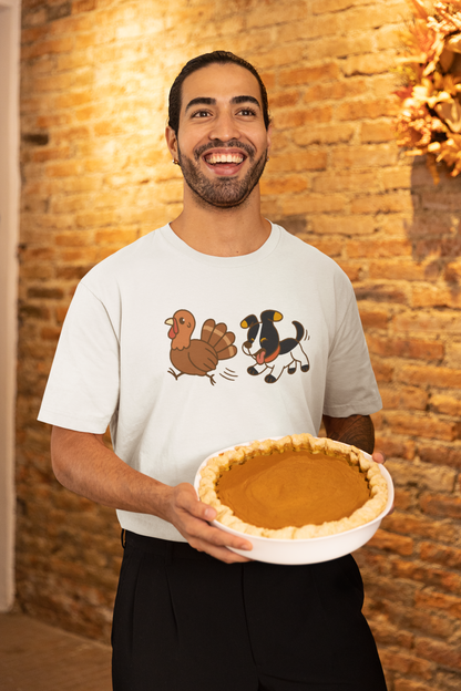 Dog Chasing Turkey T-Shirt – Funny Thanksgiving Dog Tee in white with cartoon dog and turkey, worn by smiling man