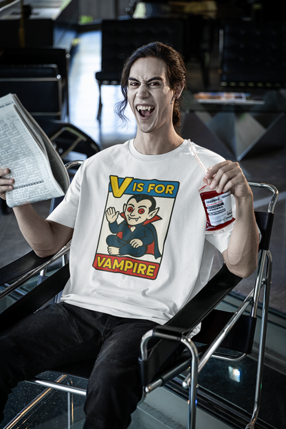 V is for Vampire T-Shirt – Funny Halloween Legend Alphabet Tee modeled by a grinning vampire man with fangs in an airport, sipping faux blood, wearing the White shirt variant