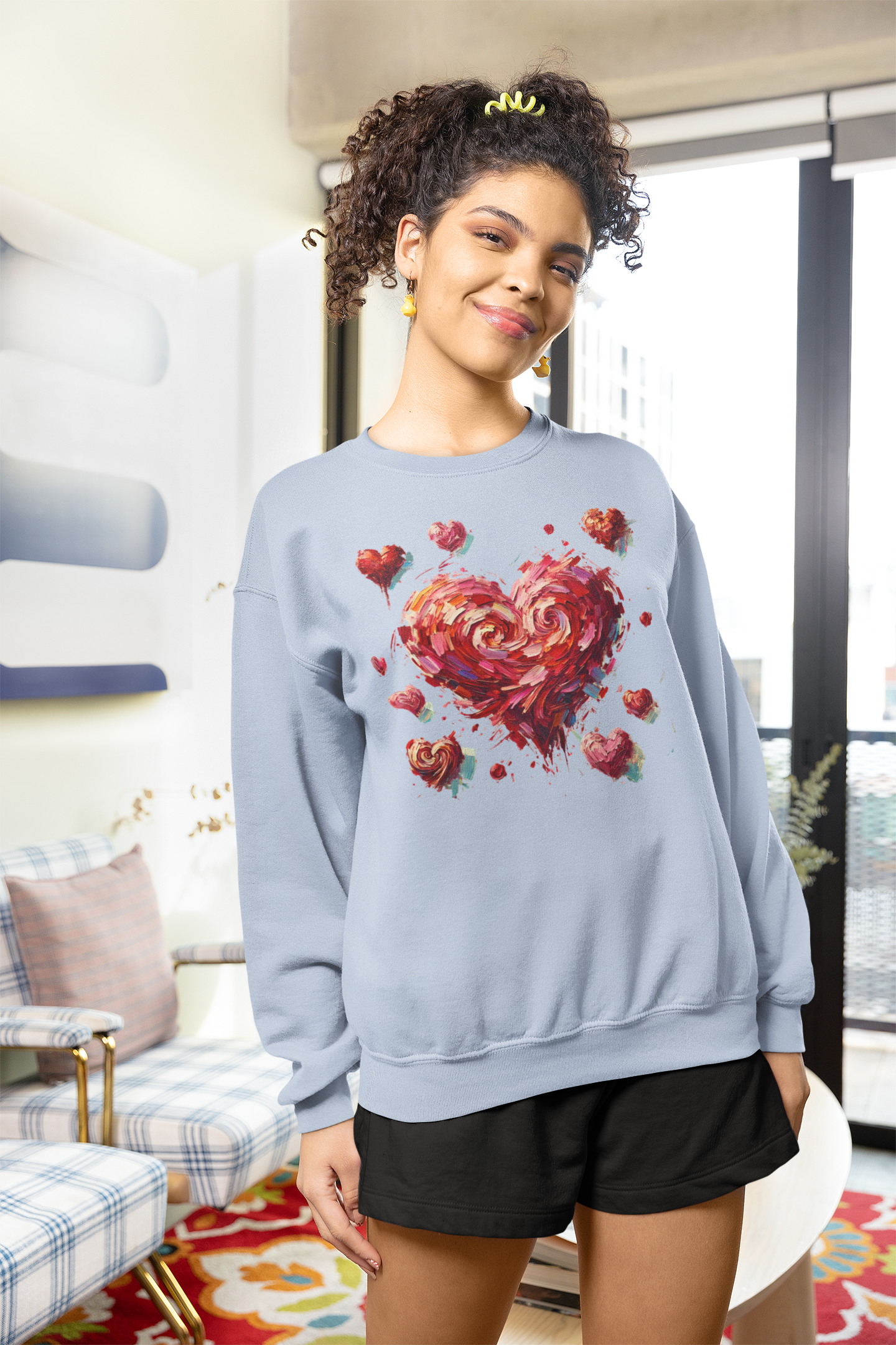 Person wearing a light blue the Impressionistic Heart Sweatshirt  with a colorful heart design in a living room.