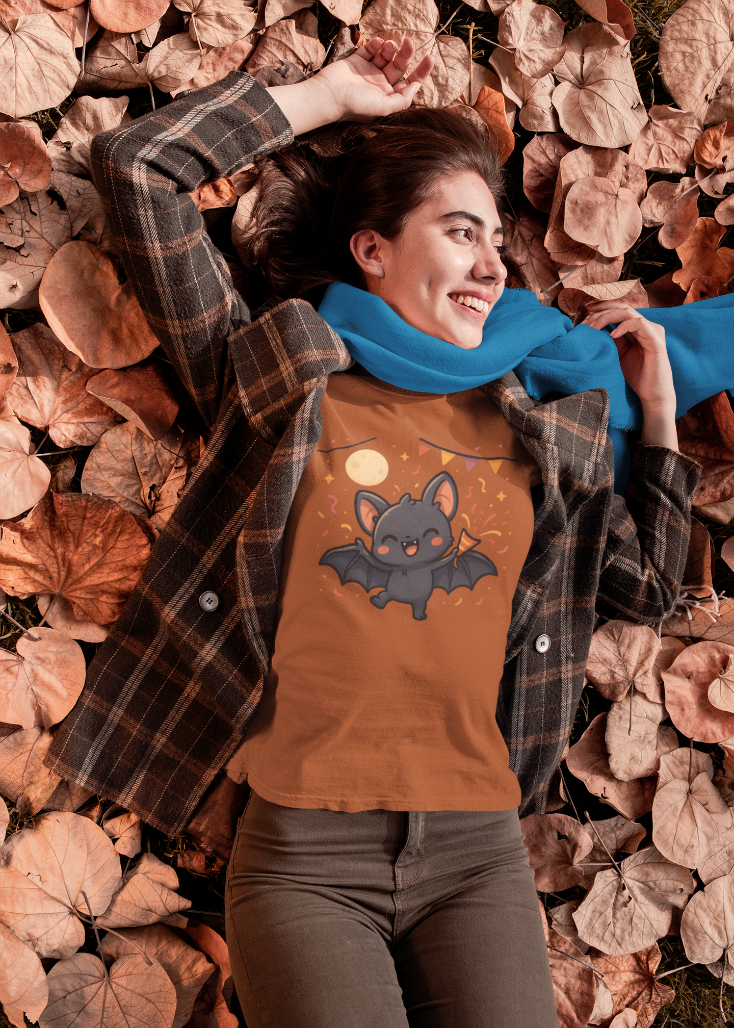 Woman wearing the Chibi Bat T-Shirt – Cute Bat Chibi Halloween Shirt for All Ages in autumn, posing in a plaid shirt with a cute chibi bat character under a full moon and orange party streamers.