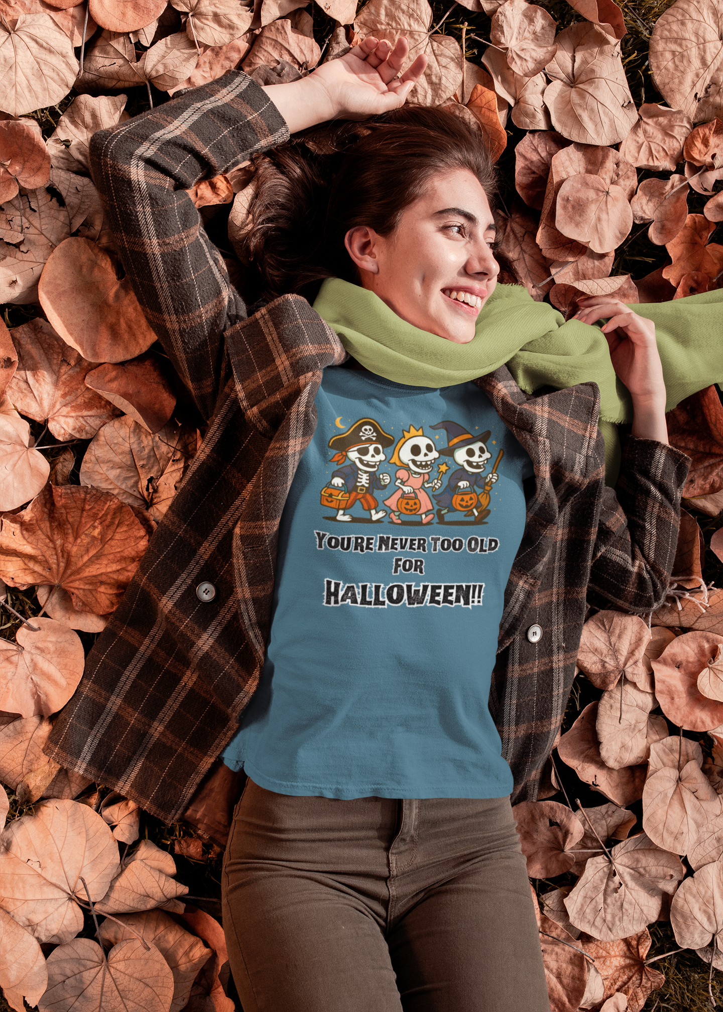 Woman lying in autumn leaves, smiling while wearing the Never Too Old for Halloween T-Shirt – Funny Adult Halloween Shirt in heather deep teal; a playful design featuring costumed skeletons stands out against the cozy fall background.
Heather Team Purple	Relaxed Fall Look – Never Too Old for Halloween Shirt	Woman in a plaid jacket and scarf relaxing in dried leaves, wearing the Never Too