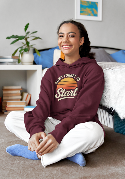 Don’t Forget to Start Hoodie – Retro Sunrise Motivational Sweatshirt in burgundy, shown in a cozy living room environment highlighting the soft fabric and inspirational design.