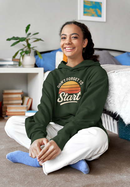 Don’t Forget to Start Hoodie – Retro Sunrise Motivational Sweatshirt in green, displayed in a casual home setting with the motivational sunrise artwork front and center.