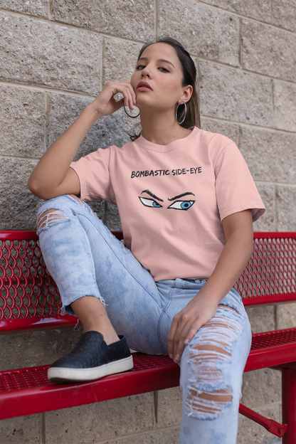 A woman in a pink Bombastic Side-Eye T-Shirt – Comic Book Style Meme Graphic Tee in pink, sitting on a red bench and highlighting the sharp comic-style eye design.