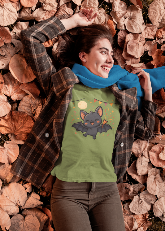 Smiling woman lying on fallen autumn leaves wearing the Chibi Bat T-Shirt – Cute Bat Chibi Halloween Shirt for All Ages in military green with a joyful cartoon bat and festive confetti under the moon.