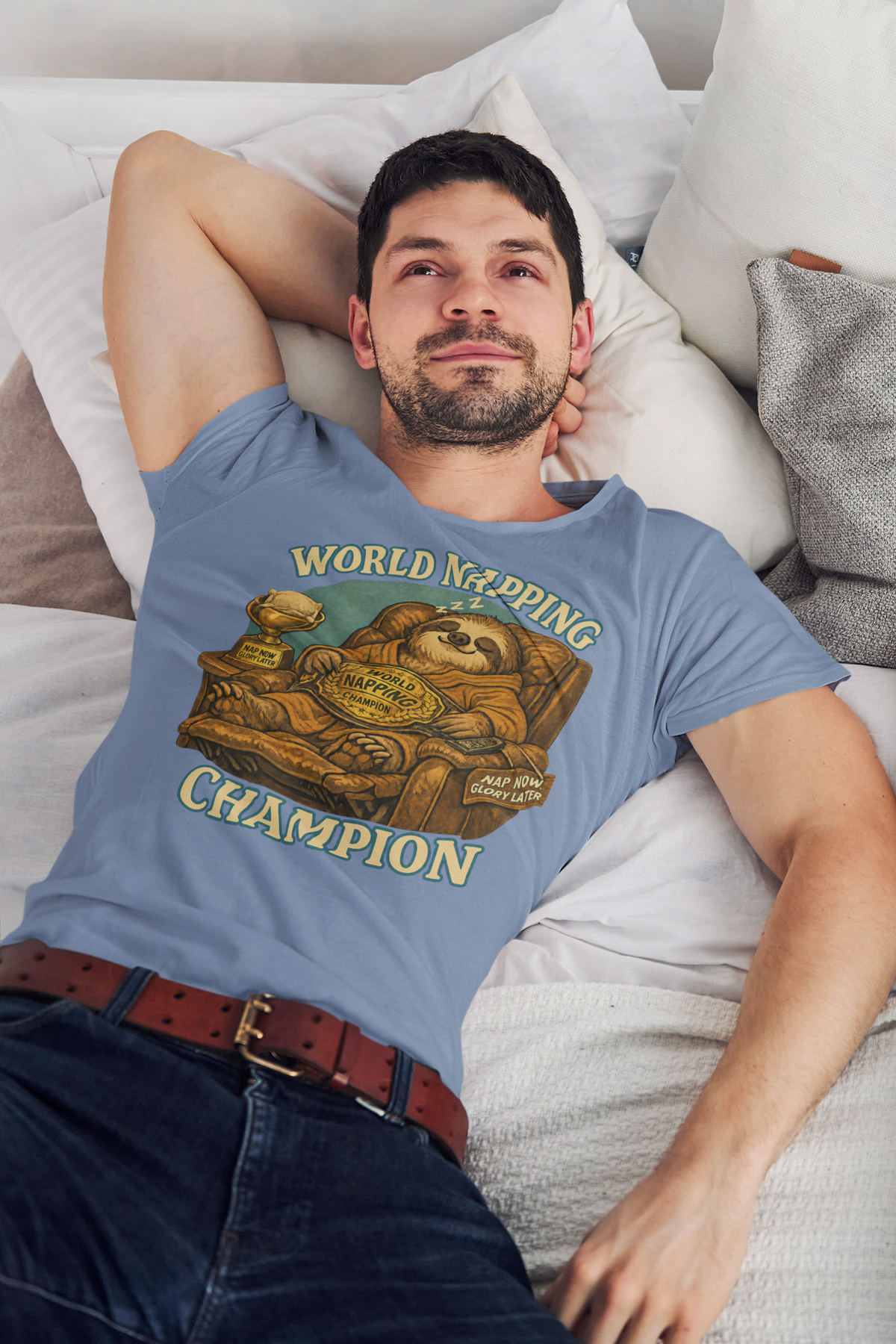 Man wearing a blue t-shirt with 'World Napping Champion' graphic, lying on a couch. The graphic is of a napping sloth in a lounge chair wearing a world champion belt