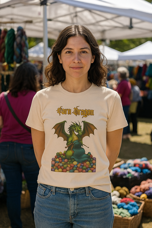 Yarn Dragon T-Shirt – Funny Knitting Dragon Shirt for Yarn Lovers shown on woman at outdoor fiber market in soft cream surrounded by skeins of yarn.