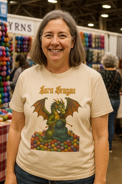 Yarn Dragon T-Shirt – Funny Knitting Dragon Shirt for Yarn Lovers worn by woman at indoor yarn festival in soft cream with colorful yarn ball display in background.
