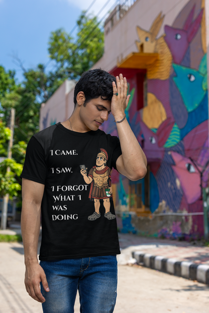 a man wearing a black I Came, I Saw, I Forgot T-Shirt – Funny ADHD t shirt from WhimSpin with text and graphics, standing in front of a colorful mural. he has his hand raised to his forehead as if he is just remembering something he forgot.