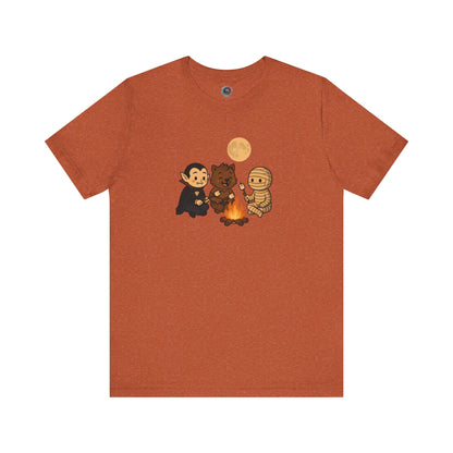 Flat lay of the Heather Autumn Halloween Monsters Campfire T-Shirt, perfect for spooky season with cartoon monsters enjoying a fall night around the fire.