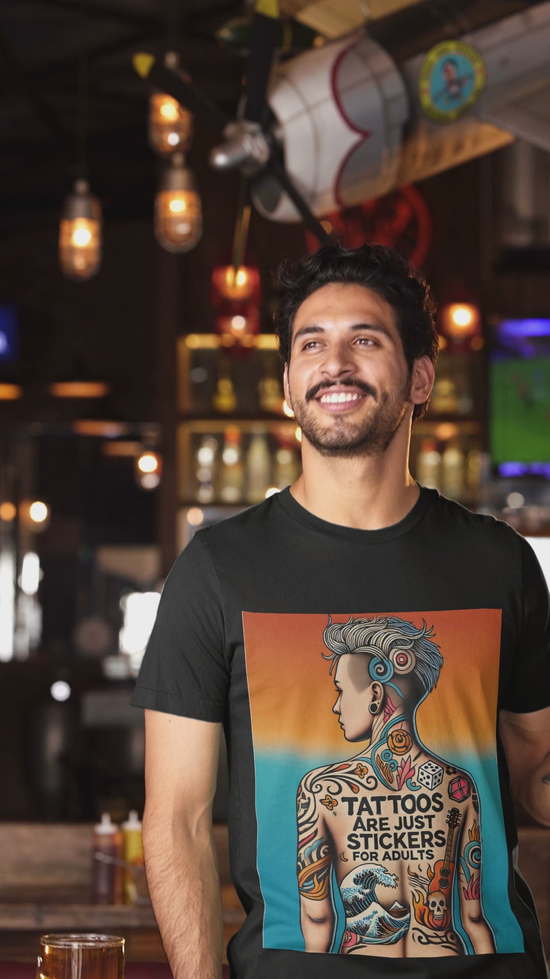 A man wearing a black Tattoos Are Just Stickers for Adults t shirt is at a bar holds a large glass of beer and smiles
